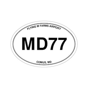May include: An oval-shaped white sticker with a thin black border. The text reads FLYING M FARMS AIRPORT in an arc at the top, MD77 in large bold black letters in the center, and COMUS, MD in smaller black text at the bottom of the sticker.