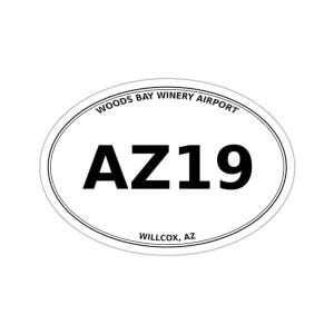 May include: An oval-shaped white sticker with a thin black border. The text "WOODS BAY WINERY AIRPORT" is printed in black along the top curve. The large black text "AZ19" is centered, and "WILLCOX, AZ" is printed in black at the bottom.