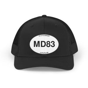 May include: A black trucker hat featuring a white oval patch on the front. The patch displays the text TY-TI-TO AIRPORT at the top, MD83 in large bold letters in the center, and LA PLATA, MD at the bottom. The cap has a solid front and mesh back.