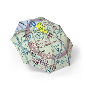 May include: A collapsible umbrella featuring a detailed aeronautical sectional chart print. The canopy displays various aviation navigation symbols, text including Okeechobee County, and a prominent yellow arrow against a pale green background.