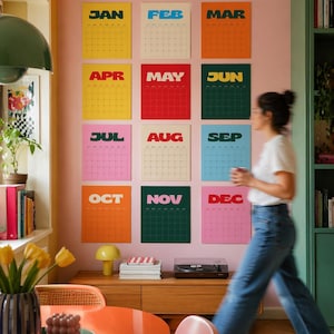 May include: A wall calendar set consisting of twelve individual rectangular prints, each representing a month from January to December. Each print features a bold, colorful background with a distinct month name in large letters and a grid layout.