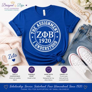 Può includere: T-shirt blu reale con un design circolare bianco che recita "THE ASSIGNMENT I UNDERSTOOD ZΦB 1920". Una tazza bianca con "Zeta" e un cuore è accanto alla maglietta. La maglietta è abbinata a jeans e scarpe da ginnastica bianche.