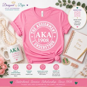 May include: A pink t-shirt with a white circular graphic that reads "THE ASSIGNMENT, AKA 1908, I UNDERSTOOD." A white mug with "AKA Excellence Sisterhood Service" is next to the shirt. The image also includes a notebook, a pen, and a pin.