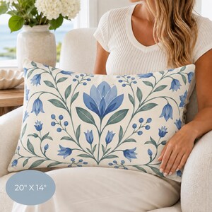 May include: A rectangular throw pillow measuring 20 inches by 14 inches, featuring a symmetrical botanical pattern of blue bell-shaped flowers, green leaves, and small blue berries on a cream-colored background with a central large blue flower.