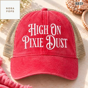 Op de afbeelding: Een rode honkbalpet met een mesh achterkant en de wit geborduurde tekst "HIGH ON PIXIE DUST" op het voorpaneel. De pet heeft een gestructureerde kroon, een gebogen klep en een knoop aan de bovenkant.