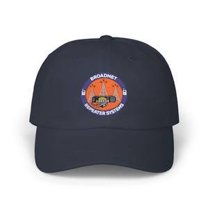 May include: Navy blue baseball cap with a circular embroidered patch. The patch features the text "BROADNET REPEATER SYSTEMS" around a design of radio towers and a radio.
