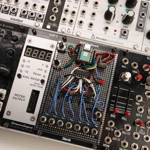 Könnte beinhalten: Nahaufnahme eines modularen Synthesizer-Panels mit verschiedenen Knöpfen, Schaltern und einer Digitalanzeige. Das Panel zeigt den Text "TEST 3", "METER OUTPUT" und "RAMPAGE". Drähte und elektronische Bauteile sind sichtbar.