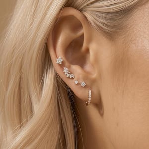 Könnte beinhalten: Ein Set aus fünf goldfarbenen Ohrringen an einem Ohr. Die Kollektion umfasst einen sternförmigen Stecker, einen fächerförmigen Stecker mit Markisenschliff, einen kleinen runden Solitärstecker, einen sechsstrahligen Stern und einen kleinen Creolen.