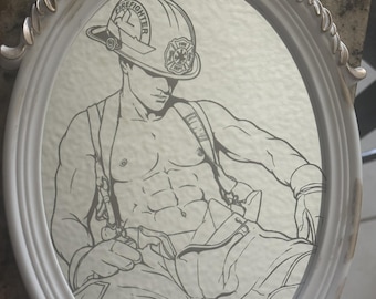 May include: An oval-shaped white and gold decorative frame containing a black and white line drawing of a shirtless firefighter wearing a helmet with the text FIREFIGHTER and a fire department emblem. The figure wears suspenders and trousers.
