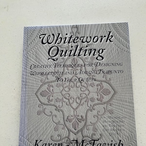 May include: A book titled "Whitework Quilting" with a gray and white quilted design on the cover. The book's title and author, Karen McTavish, are prominently displayed. The book's subtitle describes creative techniques for designing wholecloth and adding trapunto to quilts.