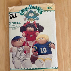 May include: A Butterick sewing pattern envelope for Cabbage Patch Kids clothes, model 6827. The front features illustrations of three dolls wearing a baseball uniform, a cheerleader outfit, and a football jersey with the number 10, plus a football.