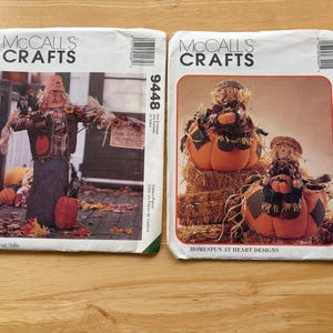 May include: Two McCall's Crafts sewing pattern envelopes. One features a scarecrow with a pumpkin, the other shows scarecrows on pumpkins. The patterns are for Homespun at Heart Designs. The envelopes have a white background with the McCall's Crafts logo.