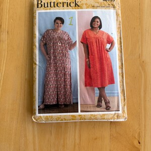 May include: A Butterick sewing pattern envelope featuring two women modeling dresses. The dresses are a floral print and a solid orange. The envelope is on a wooden surface.