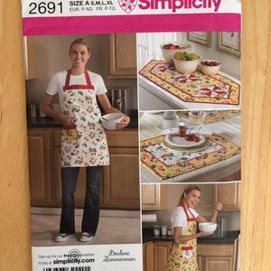 May include: Simplicity sewing pattern 2691 for an apron, table runner, and placemats. The pattern features a white fabric with a cherry print, red polka dot straps, and yellow pockets. The envelope displays finished items in a kitchen setting.