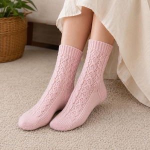 May include: A pair of light pink mid-calf socks featuring a vertical cable knit pattern on the front and sides, with a ribbed cuff at the top and a smooth knit finish on the heel and toe sections, crafted from a soft, textured knit fabric.