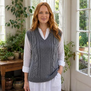 May include: A grey sleeveless V-neck sweater vest featuring a vertical cable knit pattern on the front, layered over a white long-sleeved button-down shirt. The sweater vest has a ribbed hem and ribbed trim along the neckline and armholes.