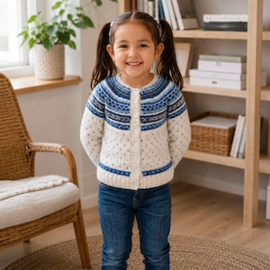 May include: A cream-colored knit cardigan featuring a blue and grey Fair Isle pattern across the chest and shoulders. The long-sleeved sweater has a round neckline, a front button closure with white buttons, and a textured knit design throughout.