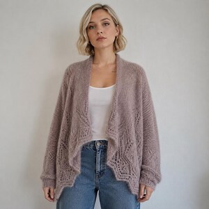 May include: A dusty mauve open-front cardigan featuring a delicate, intricate lace-like knit pattern along the front panels and sleeves. The garment has long sleeves with ribbed cuffs and a relaxed, draped silhouette, worn over a white tank top.
