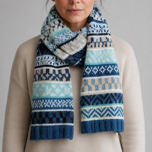 May include: A knit scarf featuring a multi-coloured fair isle pattern in shades of navy blue, light blue, turquoise, white, and beige. The scarf has a ribbed texture at the ends and displays horizontal bands of geometric shapes and snowflake motifs.