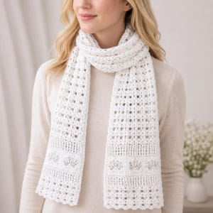 May include: A white crocheted scarf featuring an intricate openwork pattern throughout the length, with a distinct section near the ends displaying a repeating shell motif bordered by horizontal rows of delicate, airy, and textured stitching.