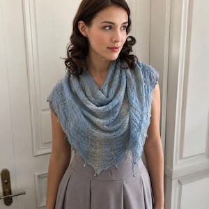 May include: A light blue triangular knit shawl featuring an intricate openwork lace pattern with subtle metallic threading throughout. The edges of the shawl are finished with small, delicate beads attached at the points of the fabric.