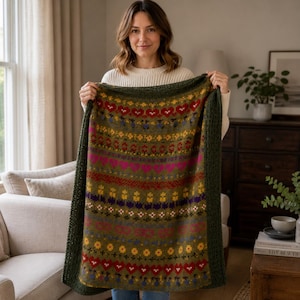May include: A rectangular knit blanket featuring a multi-colored fair isle pattern with horizontal bands of hearts, flowers, and geometric shapes in shades of olive green, red, yellow, pink, and purple, finished with a dark olive green border.