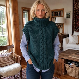 May include: A dark teal sleeveless knit sweater vest featuring a prominent vertical cable knit pattern down the centre, a thick ribbed turtleneck collar, and wide ribbed armholes, worn over a light blue long-sleeved button-down shirt and jeans.