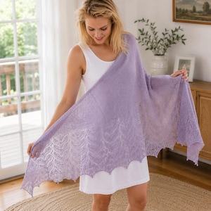 Peut inclure: Un châle tricoté de couleur violet clair présentant un motif en dentelle délicat le long du bord inférieur. Le châle est drapé sur une robe sans manches blanche unie, mettant en valeur le design ajouré complexe et la texture douce du tricot.