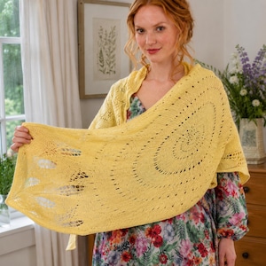 Puede incluir: Un chal tejido de color amarillo brillante que presenta un intrincado patrón de encaje con detalles calados. El chal tiene una forma semicircular con un diseño de puntadas delicado y repetitivo que irradia desde el centro, mostrando la textura del hilo.