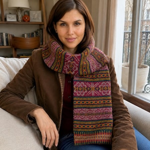 May include: A long knit scarf featuring a repeating geometric and floral pattern in shades of magenta, mustard yellow, forest green, and dark brown. The scarf has a thick, textured weave and is draped around the neck, displaying a consistent color palette.