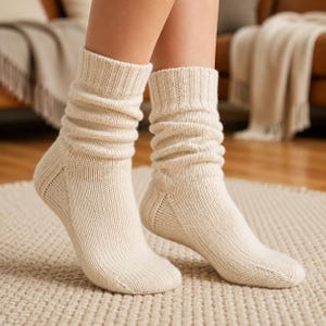May include: A pair of cream-colored, mid-calf length knit socks featuring a ribbed texture throughout the leg and foot. The socks have a slouchy, relaxed fit around the ankles and a reinforced heel construction, crafted from a soft, textured yarn.