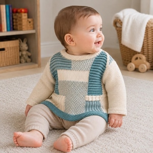 Op de afbeelding: Een baby-trui met lange mouwen en een color-block ontwerp in crème en blauwgroen met gevarieerde breistructuren, waaronder ribbel- en parelsteekpatronen, gecombineerd met een bijpassende crème-kleurige gebreide legging voor een gecoördineerde set.