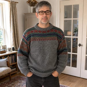 May include: A grey long-sleeve jumper featuring a round neckline and a decorative yoke pattern. The yoke displays horizontal bands of geometric shapes in shades of rust orange, dark blue, and green, contrasting against the solid grey knit body.