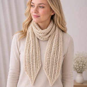 May include: A cream-coloured, open-knit scarf featuring a delicate, airy texture with vertical ribbed patterns and pointed, triangular ends. The scarf is draped loosely around the neck, showcasing a lightweight, semi-sheer construction.