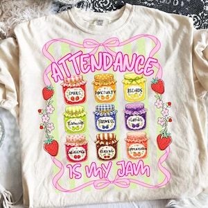 Può includere: Una t-shirt color crema con una grafica di nove barattoli di marmellata colorati etichettati con parole come Emails, Punctuality e Records. Il design include nastri rosa, fragole e il testo Attendance Is My Jam in rosa.