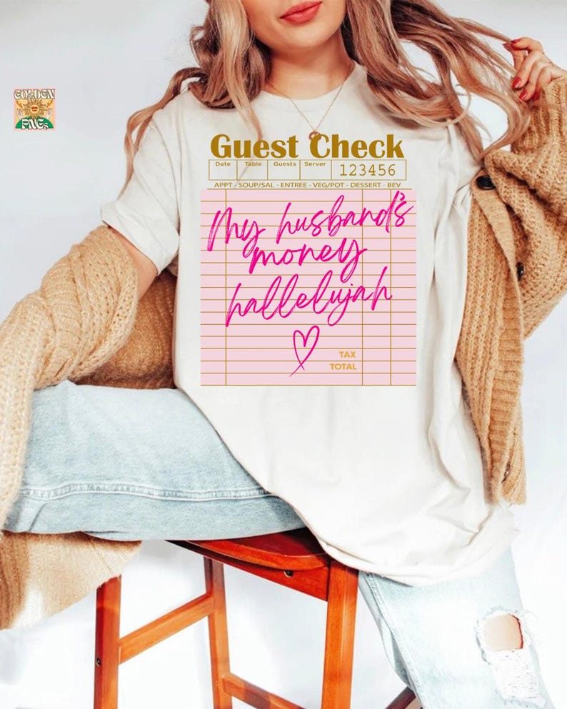 Pu&ograve; includere: Una t-shirt color crema con la grafica di un conto da ristorante. Il testo recita Guest Check 123456, My husband's money hallelujah e Tax Total, con un'icona a forma di cuore rosa. La t-shirt &egrave; indossata con un cardigan in maglia beige e jeans blu.