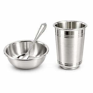 Puede incluir: Un juego de acero inoxidable pulido que consta de un cuenco pequeño y redondo, un vaso a juego con bandas horizontales y una cuchara con un patrón floral en el mango. Los artículos tienen un acabado metálico liso y reflectante.