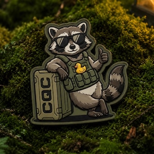 Peut inclure: Un patch représentant un raton laveur de dessin animé portant des lunettes de soleil et un gilet tactique avec un canard en caoutchouc. Le raton laveur fait un pouce levé et s'appuie sur une caisse verte avec les lettres "CQC".