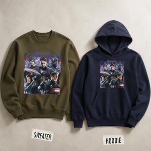 May include: An olive green crewneck sweater and a navy blue hoodie. Both feature a graphic of Captain America and the text "Captain America". The sweater and hoodie are displayed on a neutral background.