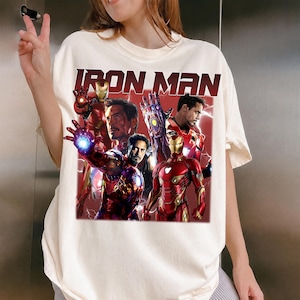Puede incluir: Camiseta color crema con un gr&aacute;fico de Iron Man en varias poses, con el texto "IRON MAN" en negrita, en rojo. El dise&ntilde;o incluye im&aacute;genes del personaje con su armadura y Tony Stark.
