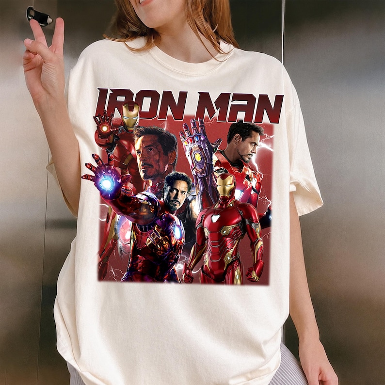 Puede incluir: Camiseta color crema con un gr&aacute;fico de Iron Man en varias poses, con el texto "IRON MAN" en negrita, en rojo. El dise&ntilde;o incluye im&aacute;genes del personaje con su armadura y Tony Stark.