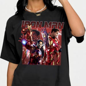 Puede incluir: Camiseta negra con la inscripci&oacute;n "IRON MAN" en rojo. El dise&ntilde;o presenta un collage de im&aacute;genes de Iron Man en su armadura roja y dorada, sobre un fondo rojo, mostrando al superh&eacute;roe.