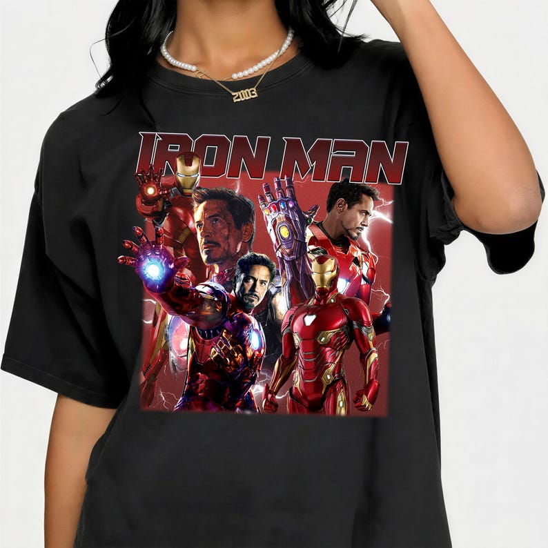 Puede incluir: Camiseta negra con la inscripci&oacute;n "IRON MAN" en rojo. El dise&ntilde;o presenta un collage de im&aacute;genes de Iron Man en su armadura roja y dorada, sobre un fondo rojo, mostrando al superh&eacute;roe.