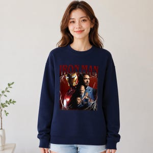 Pu&ograve; includere: Felpa girocollo blu navy con grafica di Iron Man e la scritta "IRON MAN" in rosso. La grafica include immagini del personaggio e di altre figure. La felpa &egrave; di colore unito.
