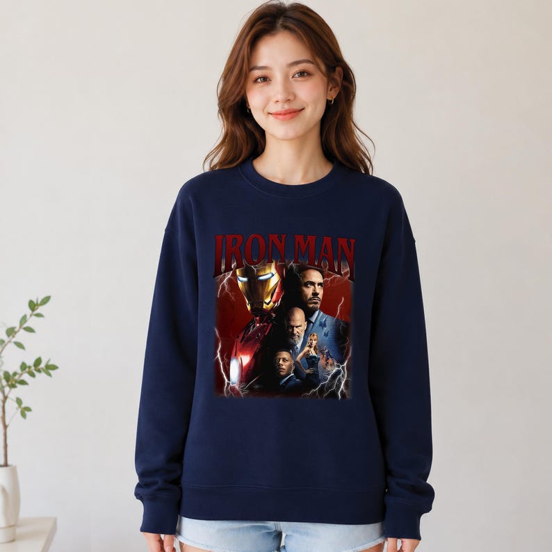 Pu&ograve; includere: Felpa girocollo blu navy con grafica di Iron Man e la scritta "IRON MAN" in rosso. La grafica include immagini del personaggio e di altre figure. La felpa &egrave; di colore unito.