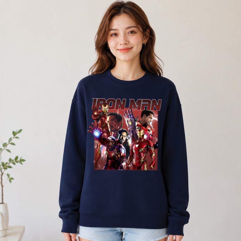 Puede incluir: Sudadera azul marino con un dise&ntilde;o de Iron Man. La imagen muestra a Iron Man en varias poses con el texto "IRON MAN" en rojo. La sudadera es de estilo casual.