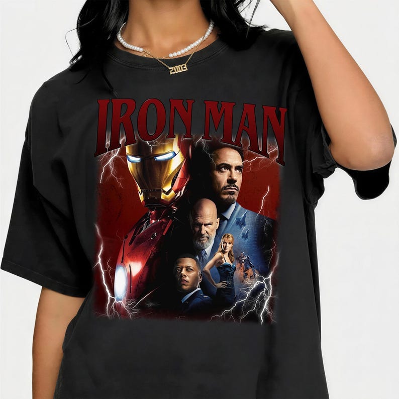 Pu&ograve; includere: T-shirt nera con una grafica di Iron Man e la scritta "IRON MAN" in rosso. Il design include immagini dell'armatura di Iron Man e dei personaggi del film, su uno sfondo di fulmini rossi e bianchi.