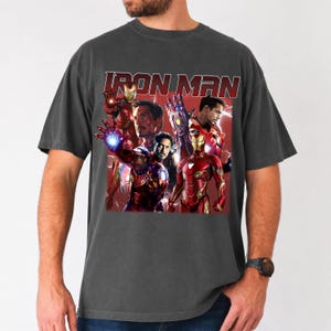 Puede incluir: Camiseta gris oscuro con un gr&aacute;fico de Iron Man y otros personajes de Marvel. El dise&ntilde;o incluye el texto "IRON MAN" en una fuente roja desgastada. La imagen tiene un aspecto vintage y descolorido.