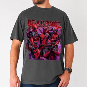 May include: Dark gray t-shirt featuring a graphic of Deadpool characters in red and black, with the word "DEADPOOL" in red block letters across the top. The design includes multiple figures in action poses.