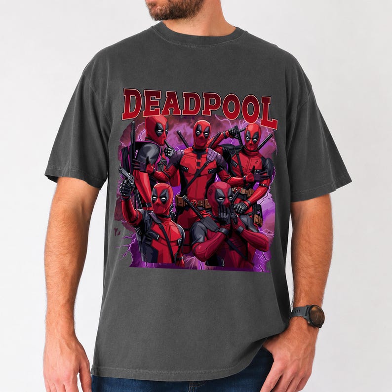 May include: Dark gray t-shirt featuring a graphic of Deadpool characters in red and black, with the word "DEADPOOL" in red block letters across the top. The design includes multiple figures in action poses.